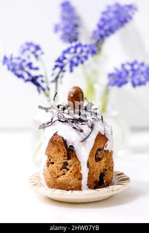Homemade traditionla Easter kulich cake with chocolate nests and eggs on ceramic plates decorated with muscari flowers on white marble table. Traditio Stock Photo
