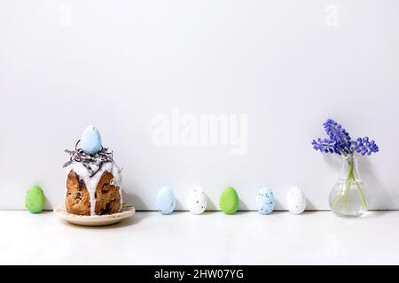 Homemade traditionla Easter kulich cake with chocolate nest and eggs on plate standing on white marble table with colored eggs in row. Traditional ort Stock Photo