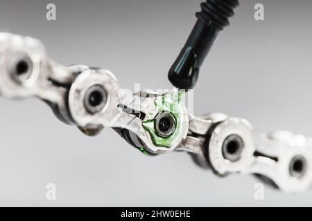 Lubricating a bicycle chain with a drop of oil close-up on an isolated gray background. Bicycle drive system maintenance Stock Photo