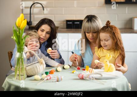 Two mothers with their children coloring Easter eggs Stock Photo