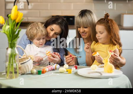 Two mothers help their children paint Easter eggs Stock Photo