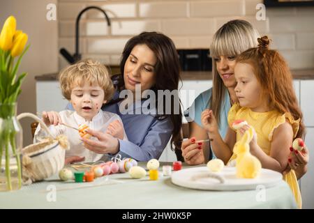 Two mothers and their children paint Easter eggs Stock Photo