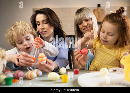 Two mothers with their children color eggs in preparation for Easter Stock Photo
