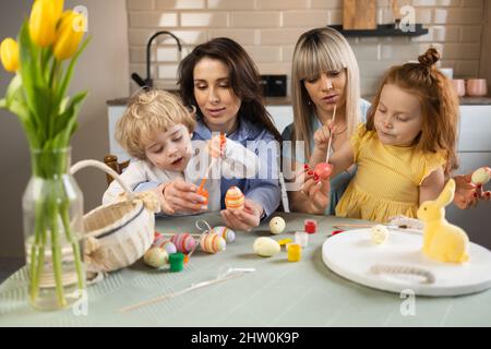 Two women and their children are sitting in the kitchen at the table and painting Easter eggs Stock Photo