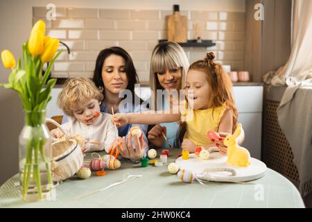 Two mothers with their children decorate Easter eggs Stock Photo
