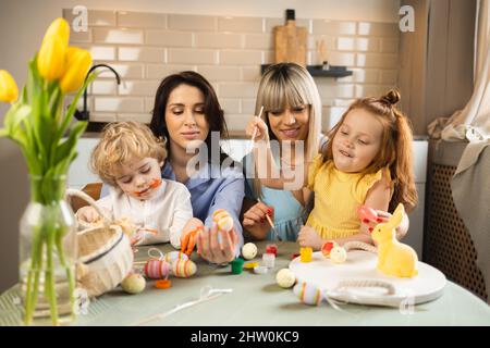 Two happy mothers with their children decorate Easter eggs Stock Photo
