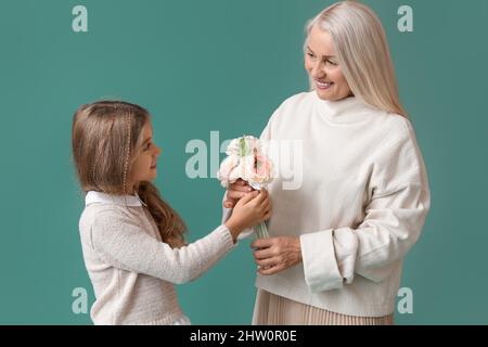 Little girl greeting her grandma with flowers on green background Stock Photo