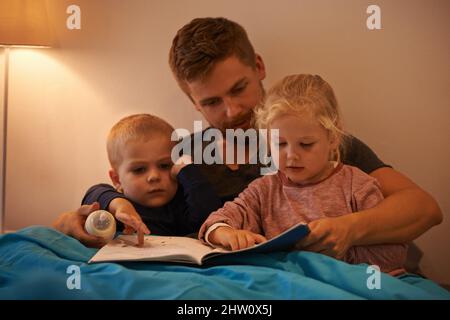 Whats that, Daddy. A father reading a bedtime story to his kids. Stock Photo