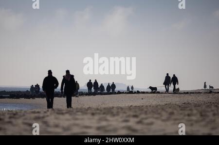 03 March 2022, Schleswig-Holstein, Föhr: Walkers are on the beach near Wyk on the North Sea island of Föhr in bright sunshine. Photo: Christian Charisius/dpa Stock Photo