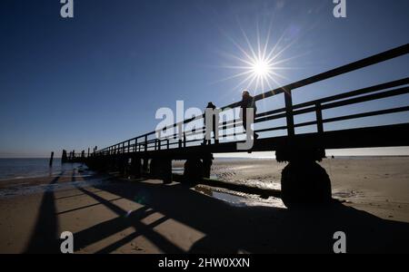 03 March 2022, Schleswig-Holstein, Föhr: Walkers are on a pier in Wyk on the North Sea island of Föhr in bright sunshine. Photo: Christian Charisius/dpa Stock Photo