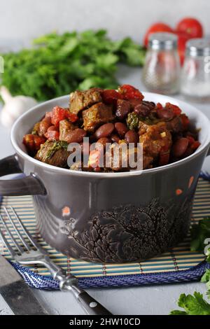 Lobio of stewed beef, red beans, onions, garlic, spices and tomatoes in a ceramic dish, Vertical format Stock Photo