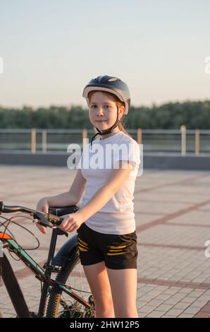 Portrait of an 11 year old girl wearing a protective bicycle helmet. Cycling along the embankment. The child is engaged in cycling Stock Photo