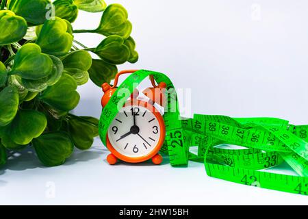 Measure tap with orange clock on white wooden background. Alarm clock set at 8 o'clock. Healthy and diet concept. Stock Photo