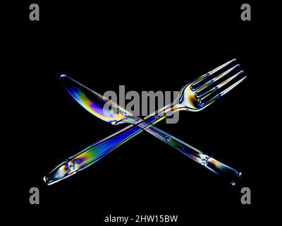 Bright rainbow stress patterns show in transparent plastic cutlery. Polarised light on a dark background. Stock Photo