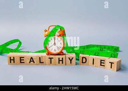 Healthy diet text on wooden block cube with measure tap and orange clock on blue background. Alarm set at 8 o'clock. Diet concept. Stock Photo