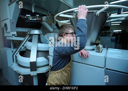 Boy with Down syndrome dressed in work clothes standing near bread makeup machine at the Dutch bakery Stock Photo
