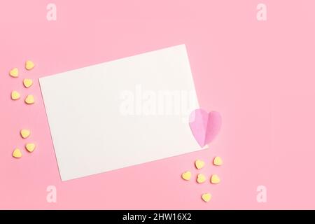 A blank white paper card with copy space and yellow candy hearts on a pink background Stock Photo