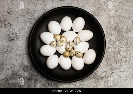 Quail and chicken eggs on a black plate on a marble background in a top view Stock Photo