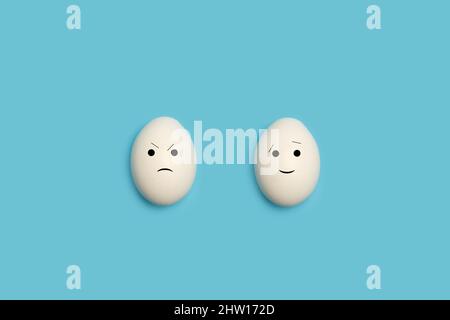 Two eggs with happy and angry face shape on a blue background Stock Photo
