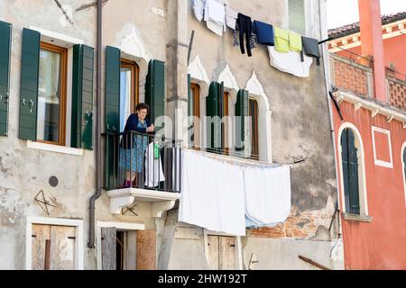 Local woman on balcony of an old medieval house over the water canal in Venice, laundry drying on the balcony, Italy Stock Photo