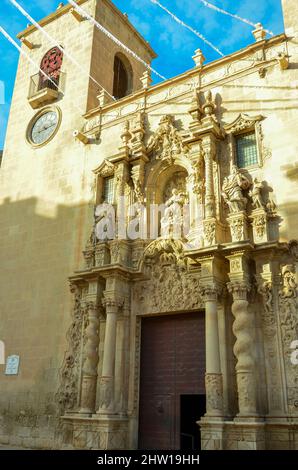 Artful entrance of the Basilica of St Mary of Alicante between the clock tower and another tower under clear blue sky. Valencian Gothic style from the Stock Photo