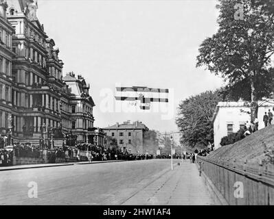 An early 20th century photograph of crowds watching English aviator and pioneer flyer  Claude Grahame-White (1879-1959) fly his Farman III biplane in front of the State, War & Navy building, Washington, D.C. USA on October 14th, 1910. The aircraft, the Farman III, also known as the Henry Farman 1909 biplane, was an early French aircraft designed and built by Henry Farman in 1909. Stock Photo