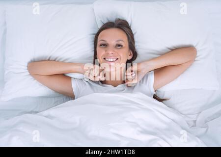Good morning. Top view of beautiful young woman wakening up happy in the bed and looking into the camera Stock Photo