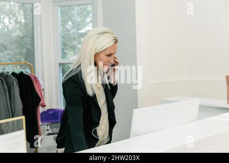 A female small business owner of a medical spa and retail shop standing behind the counter with a computer working Stock Photo