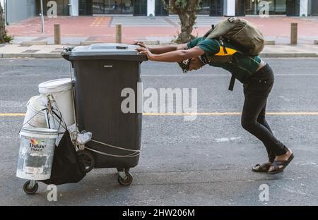 Cape Town, South Africa, 26th February - 2022: Man pushes wheelie bin and buckets full of water to wash cars. Stock Photo