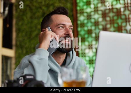 Cheerful young adult man in casual clothes in cafe talking on a mobile phone Stock Photo