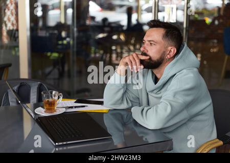 Pensive bearded man in casual clothes in cafe using his laptop Stock Photo