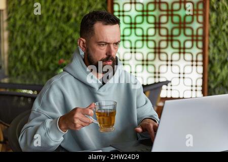 Thoughtful bearded man in casual clothes in cafe using laptop Stock Photo