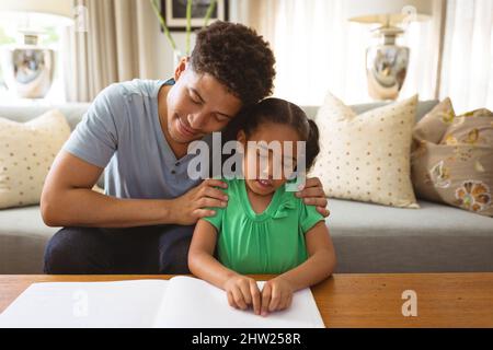 Biracial blind girl touching braille while reading book by father in living room at home Stock Photo