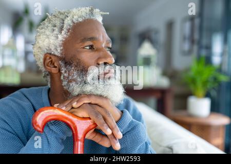 Thoughtful african american senior man looking away while leaning on walking cane at home Stock Photo