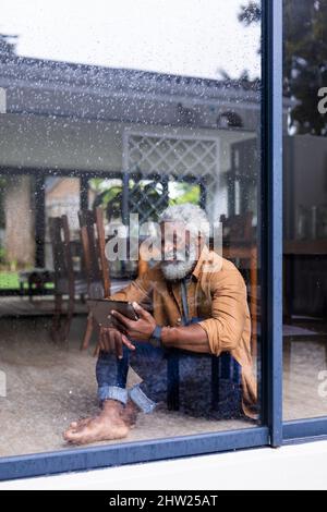 Smiling african american man using tablet pc seen through glass window at home Stock Photo