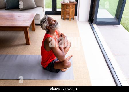 Retired african american senior man practicing yoga while sitting on mat at home Stock Photo