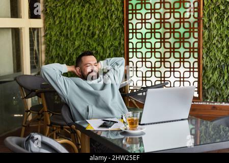 Smiling bearded man in casual clothes in cafe using laptop Stock Photo