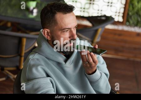 Serious young adult man in casual clothes in cafe records audio messages Stock Photo