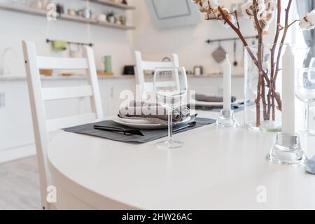 dining table with white plate setting in modern home. cotton branches are in vase. Cozy kitchen.Beautiful table setting with narcissus flowers Stock Photo