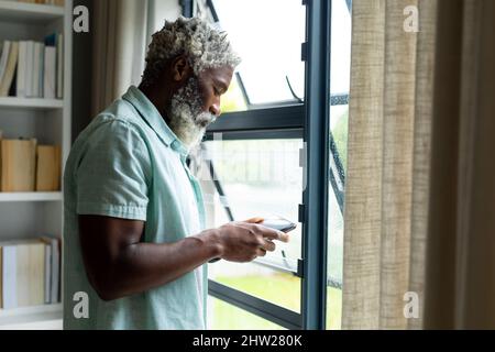 African american man using tablet pc while standing by window at home Stock Photo