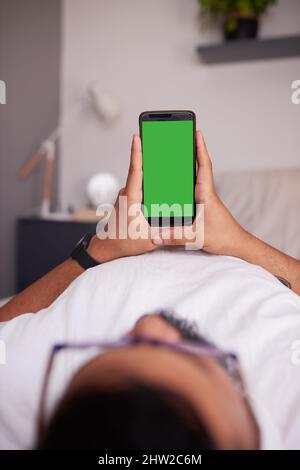 An unidentified man holds a mobile phone in his bedroom. Chroma key Stock Photo