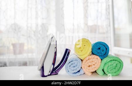 Towels folded in a roll and an iron after ironing on an ironing board. housekeeping concept Stock Photo
