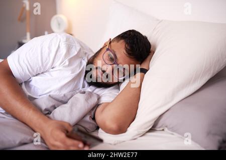 A man wearing spectacles looking at his mobile phone while lying in bed Stock Photo