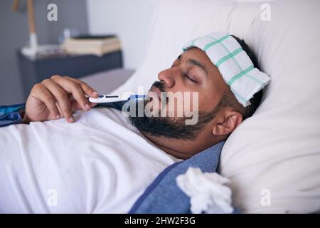 A man lies in bed with an oral thermometer unidentified reading Stock Photo