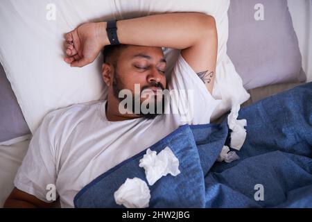 An overhead shot of a sick man sleeping in bed surrounded by tissues Stock Photo