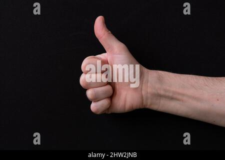 Close-up of man hand showing thumb up, on a black background. Stock Photo