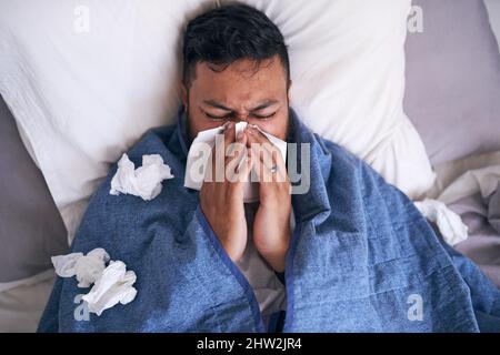 An overhead shot of a sick man blowing his nose while lying in bed Stock Photo