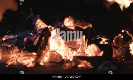 Close-up of burning black coals. Action. Burning out small flames on coals for barbecue in nature. Hot and warm burning coals for ignition. Stock Photo