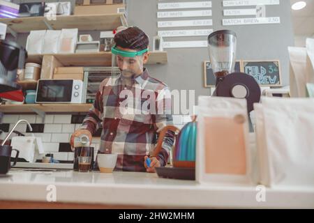 Man barista working in cafe in protective visor, preparing coffee Stock Photo
