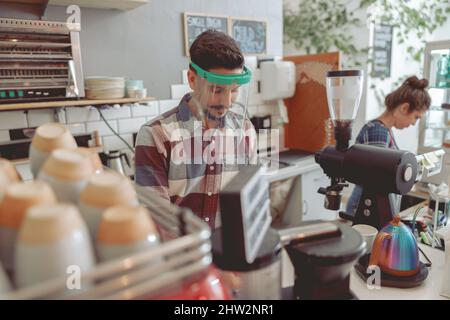 Smiling barista with mustache in protective visor preparing coffee Stock Photo